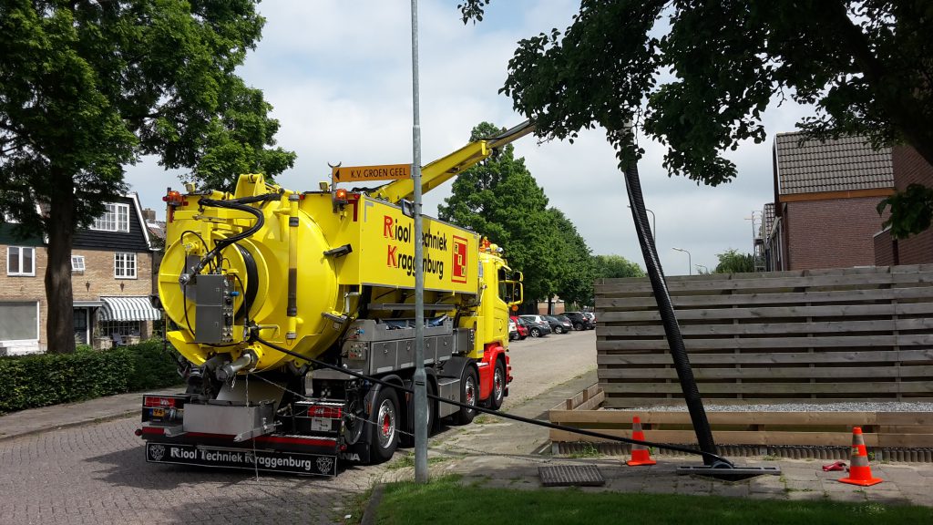 Gele rioolreiniging vrachtwagen met hogedrukspuit bij rioolonderhoud op straat tussen bomen